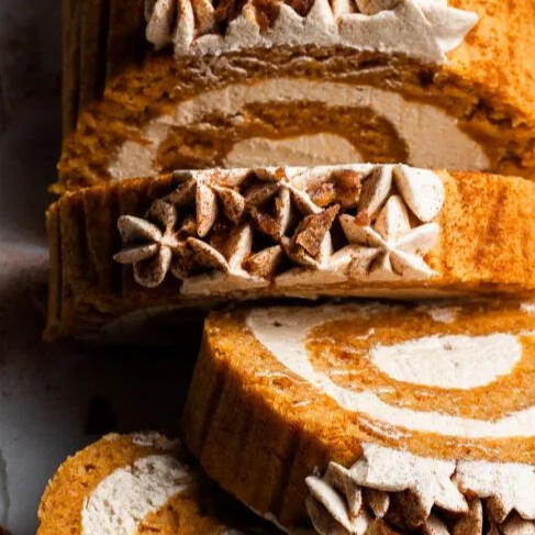 Pumpkin Roll: A decadent pumpkin flavored soft cake with vanilla cream cheese filling. Topped with piped cream cheese and cinnamon powder.
